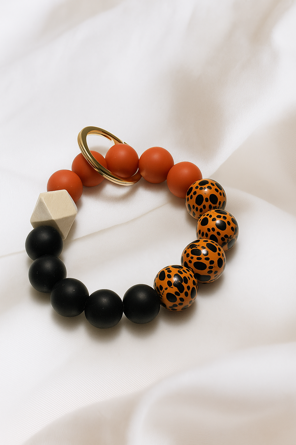 Beaded keychain with orange, black, and leopard print beads on a white fabric background